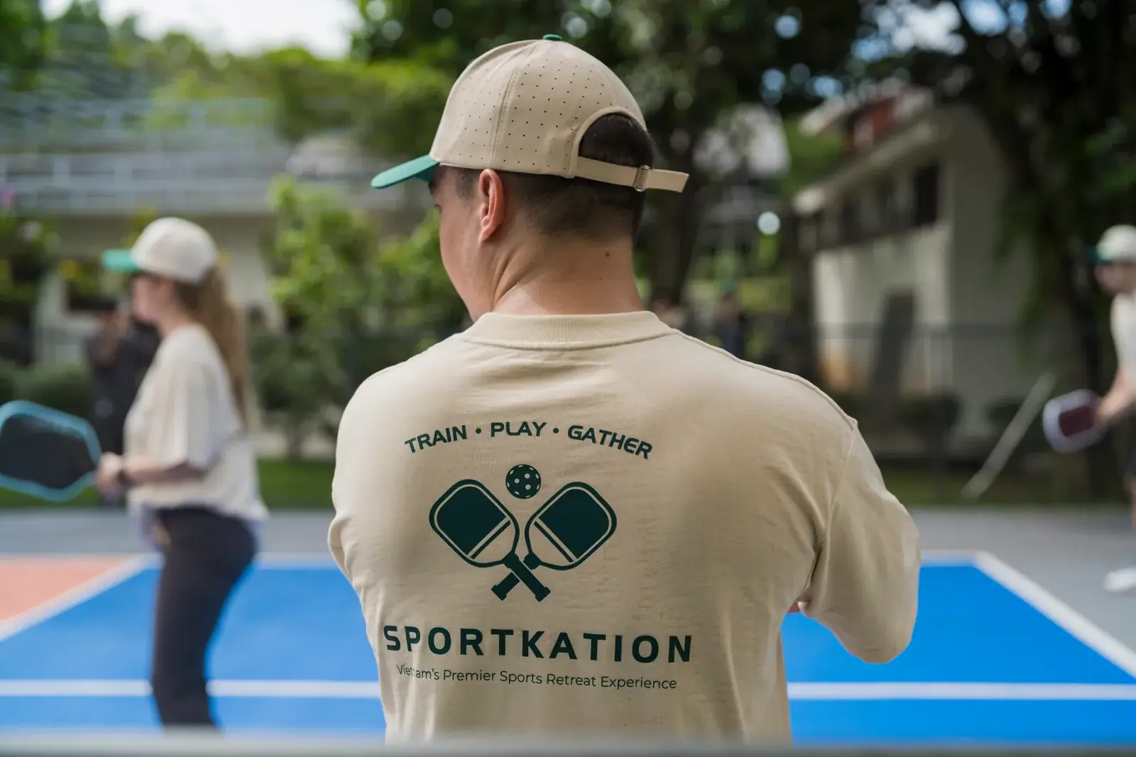A participant wearing a Sportkation shirt watching pickleball beside the court