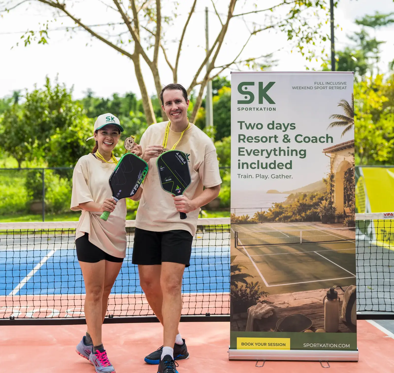 Two Sportkation participants holding paddles and medals beside the training camp banner