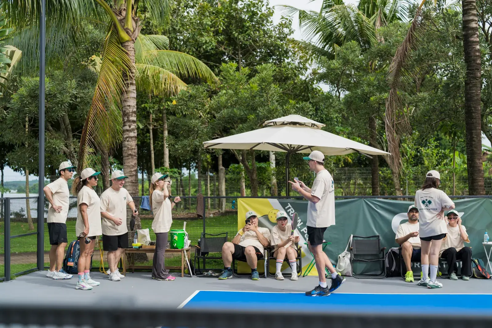 The Sportkation group resting and talking beneath an umbrella beside the courts